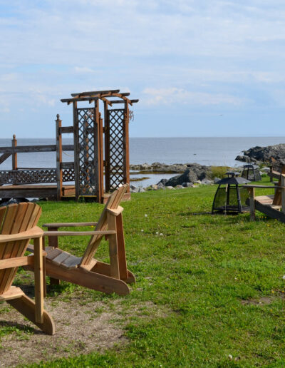 Foyer extérieur et chaises Adirondack au bord du fleuve, devant les chalets du Logis du Bois Flotté