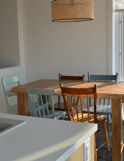 Salle à manger avec table et chaises colorées en bois, à aire ouverte sur la cuisine du chalet Le Clapotis de la marée au Logis du Bois Flotté