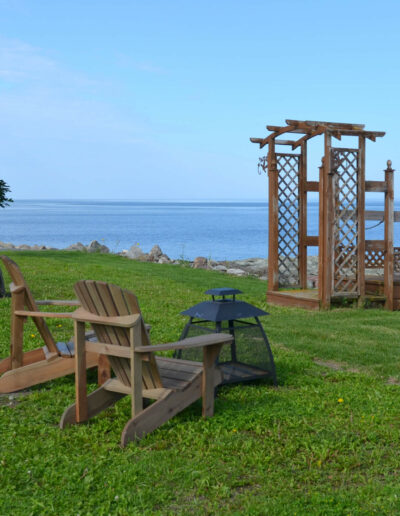 Foyer extérieur et chaises Adirondack au bord du fleuve, devant les quatre chalets du Logis du Bois Flotté